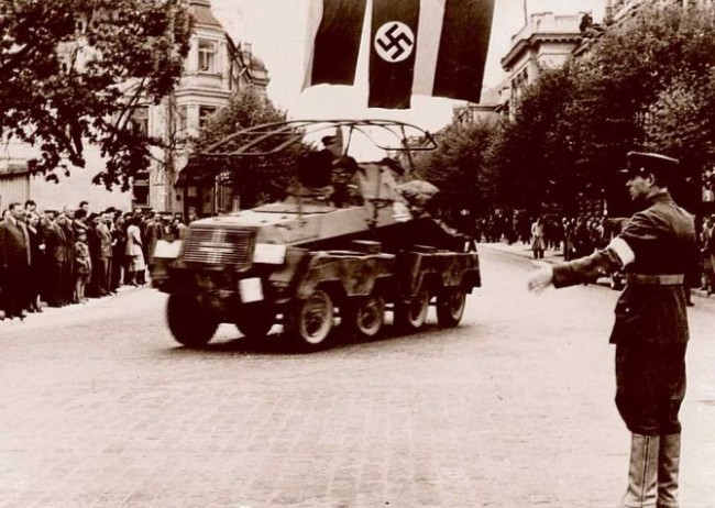 1941 m. birželio pabaigoje lietuviai patys išsikovojo laisvę, atkūrė tarpukario įstaigas ir palaikė tvarką krašte. Lietuvių policininkas rodo vokiečių kariuomenės šarvuočio įgulai kelią, kuriuo ji turi važiuoti.